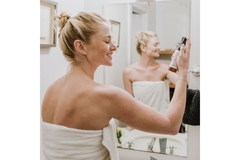 Image A woman spraying a face spray on herself in a towel in her bathroom.